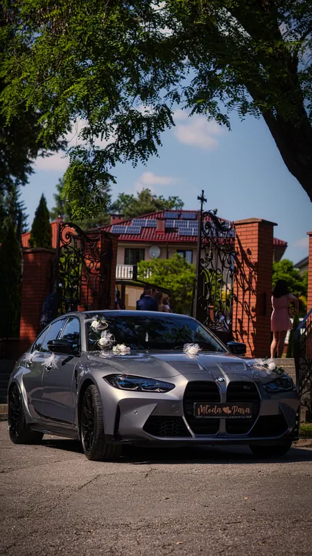 Szare BMW M3 z dekoracją ślubną przed bramą