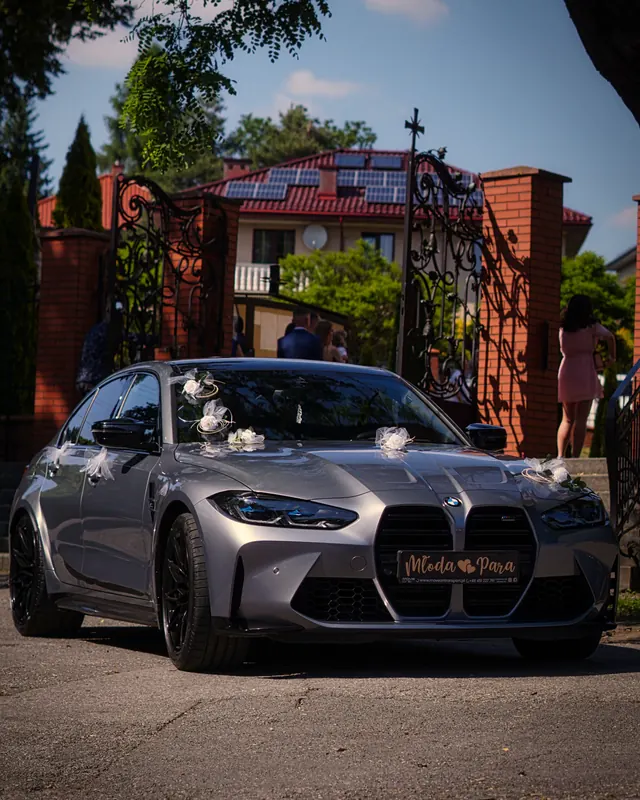 Szare BMW M3 Competition przed bramą kościoła